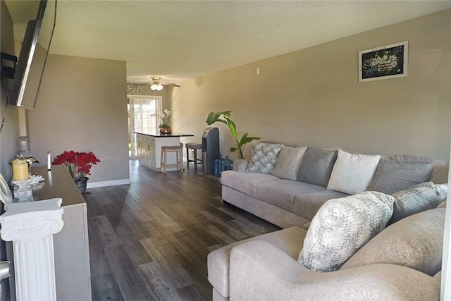 living room featuring ceiling fan, baseboards, a textured ceiling, and dark wood-style floors