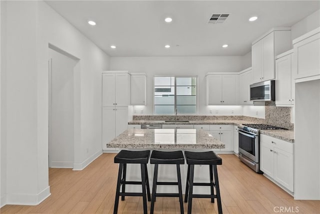 kitchen with appliances with stainless steel finishes, a kitchen island, white cabinetry, and light stone countertops