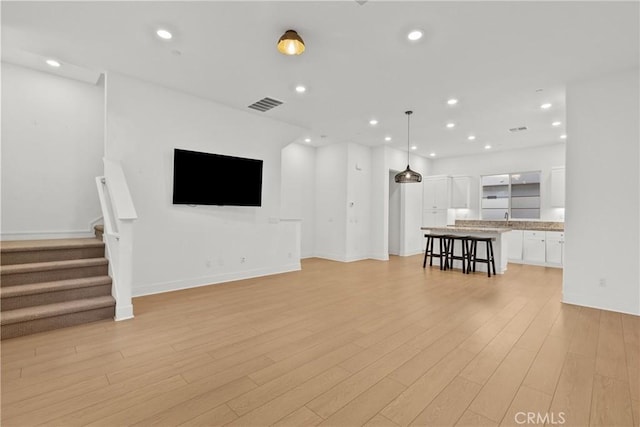 unfurnished living room featuring light wood-style flooring, stairs, visible vents, and recessed lighting