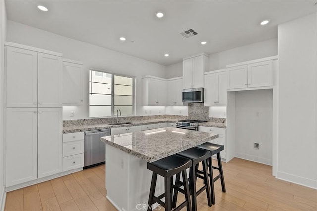 kitchen with stainless steel appliances, white cabinetry, a kitchen island, a sink, and a kitchen bar