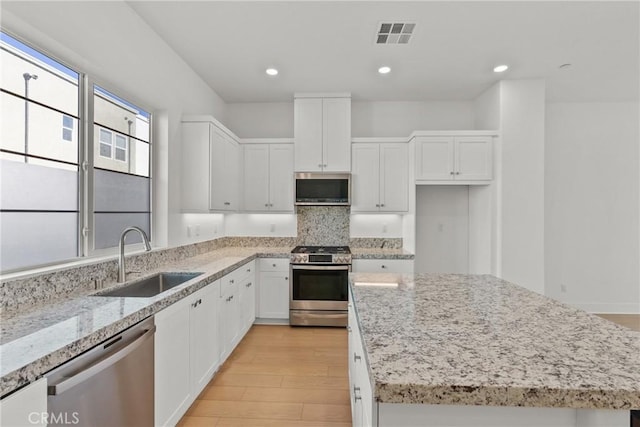 kitchen featuring stainless steel appliances, white cabinetry, a sink, a kitchen island, and light stone countertops