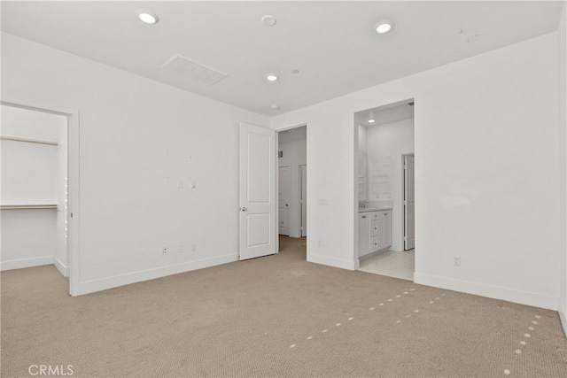 unfurnished bedroom with light carpet, baseboards, a walk in closet, and recessed lighting