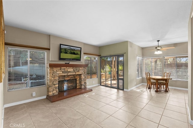 living room with light tile patterned floors, a stone fireplace, a wealth of natural light, and baseboards