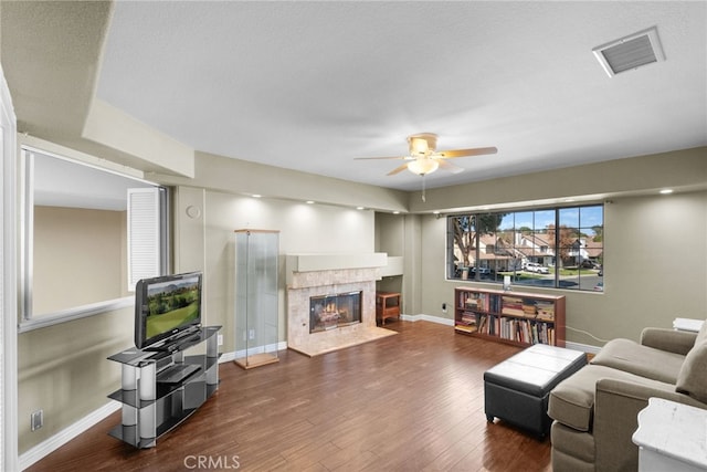 living room featuring visible vents, a ceiling fan, a glass covered fireplace, wood finished floors, and baseboards