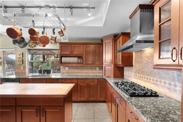 kitchen featuring brown cabinetry, wood counters, wall chimney range hood, and black gas stovetop