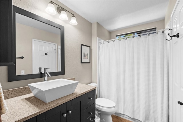 bathroom featuring a textured wall, curtained shower, vanity, and toilet