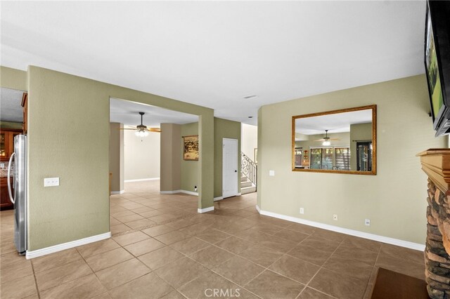 empty room featuring stairway, a ceiling fan, a stone fireplace, tile patterned flooring, and baseboards