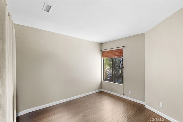 empty room with visible vents, dark wood finished floors, and baseboards