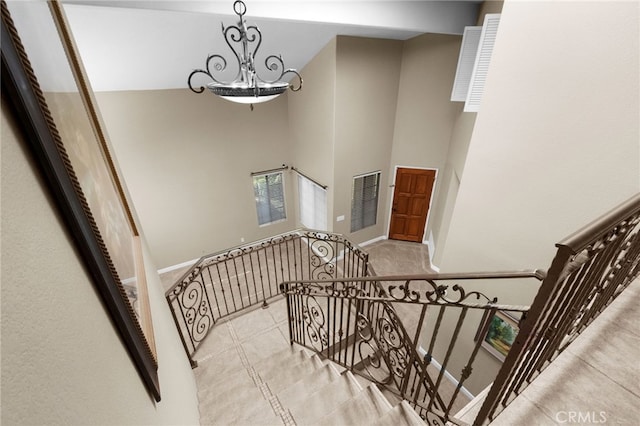 staircase with visible vents, a high ceiling, an inviting chandelier, baseboards, and tile patterned floors