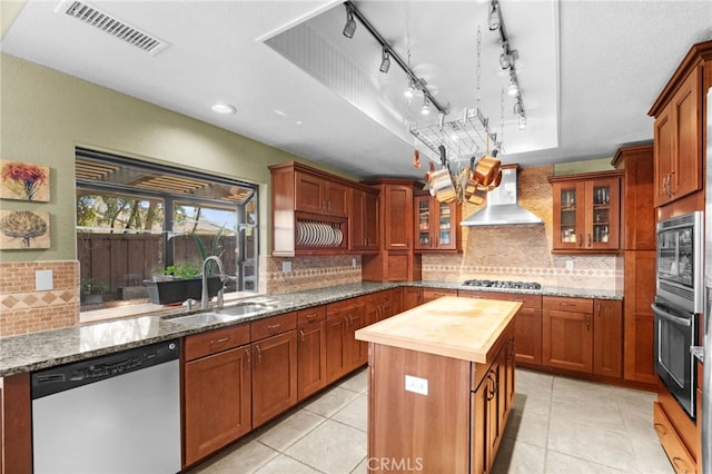 kitchen with stainless steel appliances, butcher block counters, visible vents, a sink, and wall chimney exhaust hood