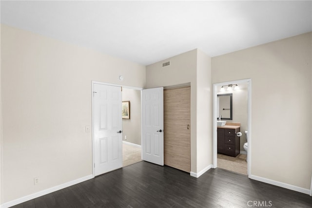 unfurnished bedroom with dark wood-style flooring, a closet, visible vents, connected bathroom, and baseboards