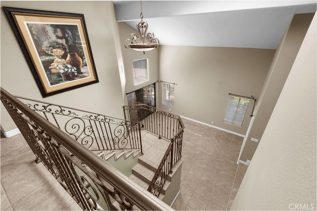 stairs with vaulted ceiling, a notable chandelier, and baseboards