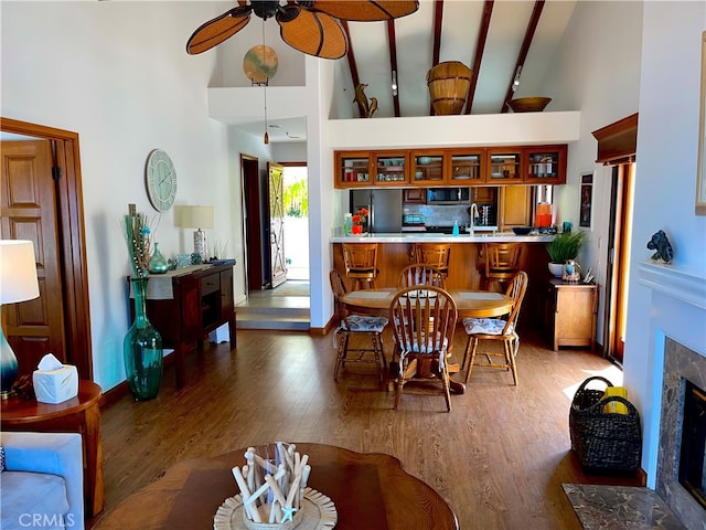 dining room with a premium fireplace, a ceiling fan, dark wood-type flooring, high vaulted ceiling, and baseboards