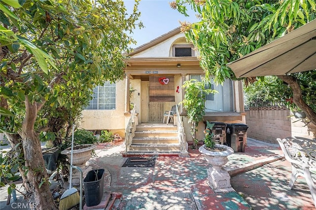 view of exterior entry with a patio area, fence, and stucco siding