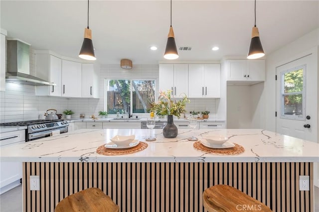 kitchen featuring a healthy amount of sunlight, gas range, wall chimney exhaust hood, and visible vents