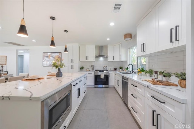 kitchen with a sink, visible vents, appliances with stainless steel finishes, wall chimney exhaust hood, and tasteful backsplash