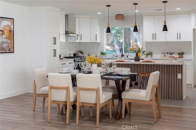 kitchen featuring light wood finished floors, light countertops, a kitchen island, wall chimney range hood, and stainless steel gas range oven