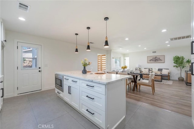 kitchen featuring visible vents, stainless steel microwave, white cabinets, and a center island