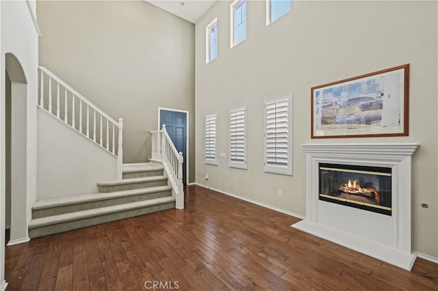 unfurnished living room featuring a towering ceiling, baseboards, stairs, wood-type flooring, and a glass covered fireplace