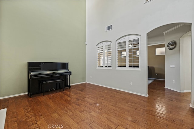 empty room featuring arched walkways, hardwood / wood-style flooring, visible vents, and baseboards