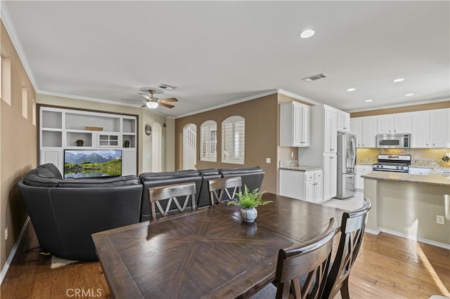 dining room with baseboards, visible vents, a ceiling fan, ornamental molding, and light wood-style floors