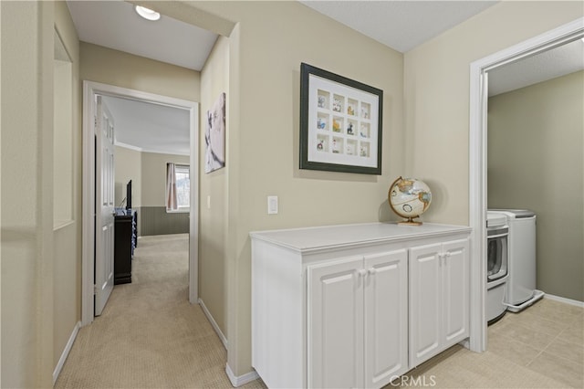 hall with light carpet, baseboards, and washer and clothes dryer