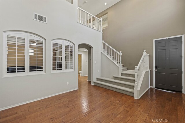 foyer with arched walkways, hardwood / wood-style flooring, visible vents, baseboards, and stairway