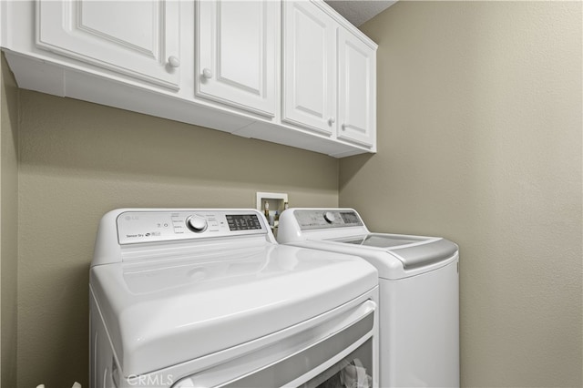 clothes washing area with cabinet space, a textured wall, and separate washer and dryer