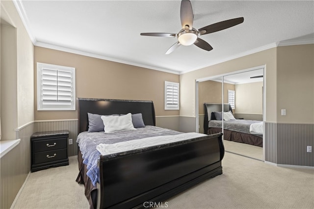 bedroom featuring light carpet, a wainscoted wall, ceiling fan, crown molding, and a closet