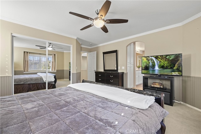 bedroom with light colored carpet, wainscoting, ceiling fan, crown molding, and a fireplace