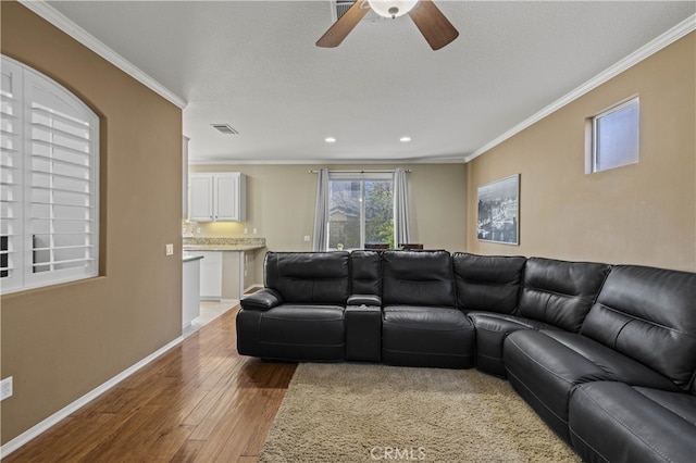 living room featuring light wood finished floors, baseboards, visible vents, a textured ceiling, and crown molding