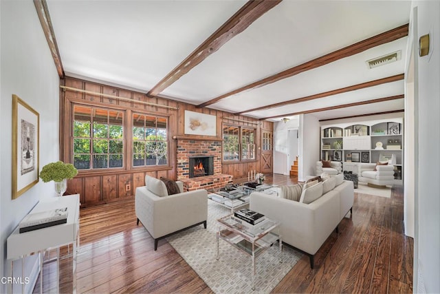 living area with a wealth of natural light, a brick fireplace, beam ceiling, and wood finished floors