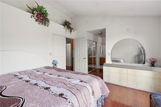 bedroom featuring vaulted ceiling, wood finished floors, and connected bathroom