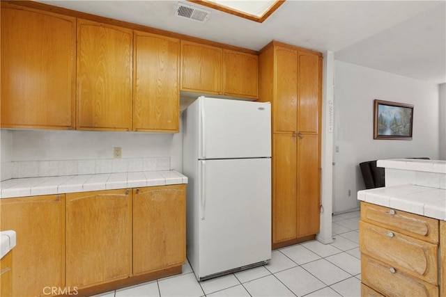 kitchen with tile counters, freestanding refrigerator, visible vents, and light tile patterned floors