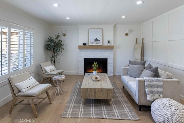 living area featuring crown molding, a fireplace, a decorative wall, and light wood finished floors