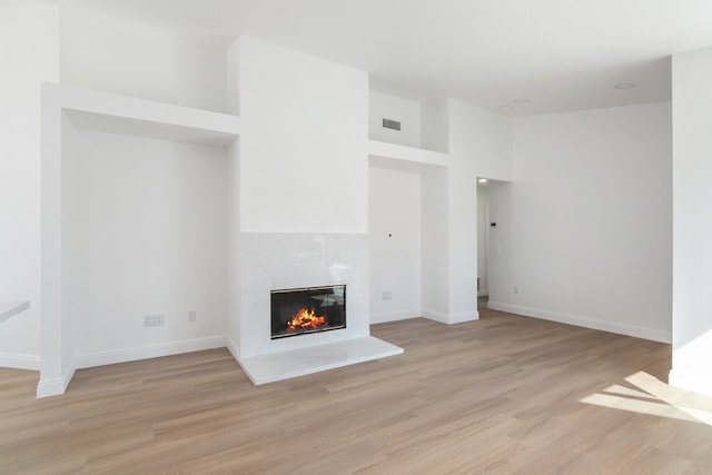 unfurnished living room with light wood-style flooring, visible vents, baseboards, and a high end fireplace