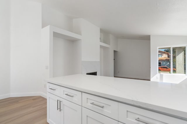 kitchen featuring light wood finished floors, baseboards, light stone counters, and white cabinets