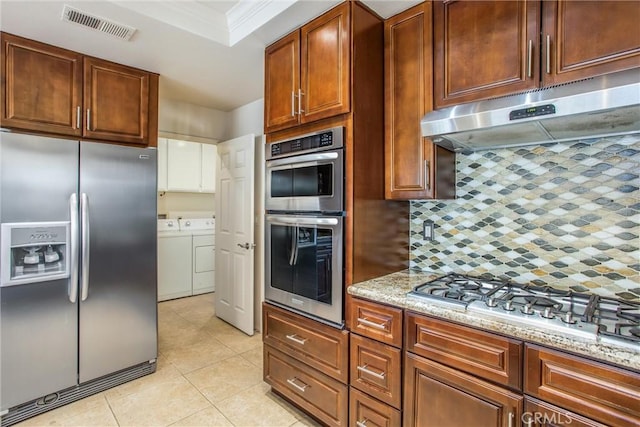 kitchen with light stone counters, under cabinet range hood, visible vents, washer and dryer, and appliances with stainless steel finishes