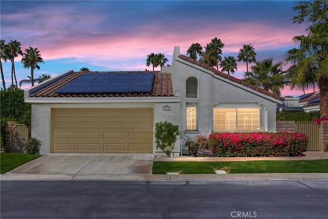 view of front of home with an attached garage, driveway, solar panels, and stucco siding