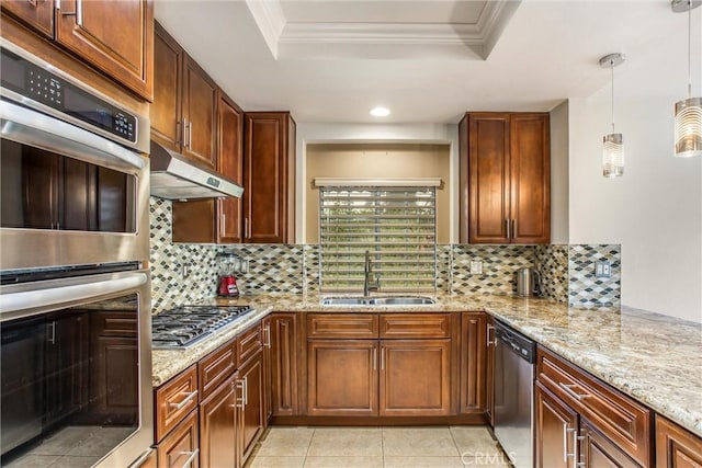 kitchen featuring a tray ceiling, stainless steel appliances, hanging light fixtures, a sink, and under cabinet range hood