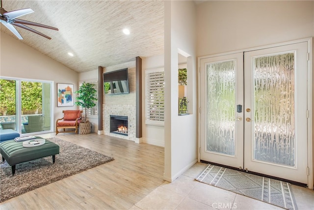 interior space with french doors, a fireplace, light wood finished floors, ceiling fan, and high vaulted ceiling