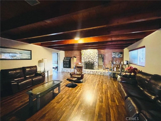 living room with beam ceiling, a stone fireplace, and wood finished floors