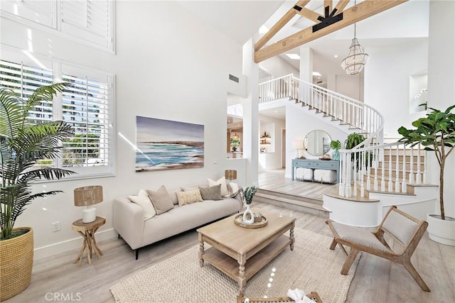 living room featuring visible vents, stairway, wood finished floors, a high ceiling, and a chandelier