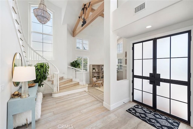 entrance foyer with a towering ceiling, visible vents, stairs, light wood-type flooring, and beam ceiling