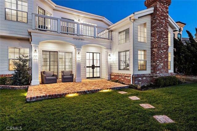 rear view of property with a balcony, a patio area, a chimney, and a yard