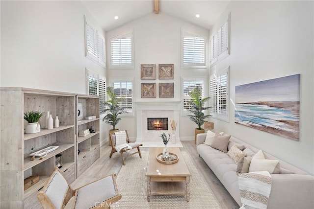 living area featuring high vaulted ceiling, beamed ceiling, light wood-type flooring, and a fireplace with flush hearth