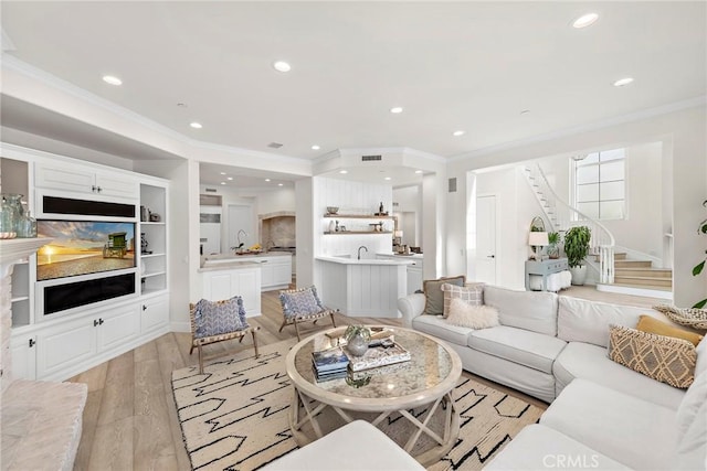 living room featuring ornamental molding, recessed lighting, light wood finished floors, and stairs