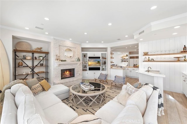 living area featuring visible vents, light wood-style flooring, ornamental molding, a brick fireplace, and recessed lighting