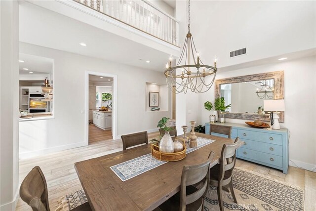 dining room featuring a towering ceiling, baseboards, visible vents, light wood-type flooring, and an inviting chandelier