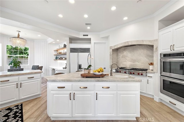 kitchen with stainless steel appliances, white cabinetry, light countertops, light wood finished floors, and an island with sink